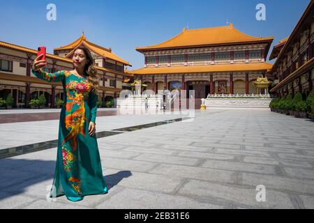 Ragazza vietnamita in tradizionale ao dai che prende un selfie durante Anno nuovo cinese al tempio Fo Guang Shan di Bangkok Foto Stock