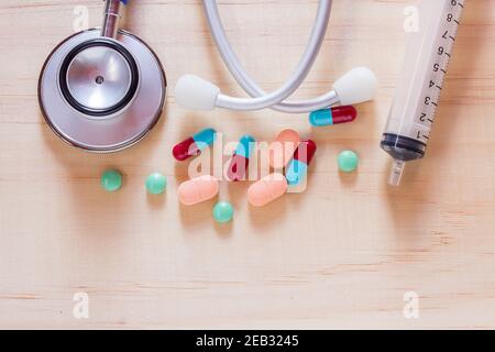 Siringa, stetoscopio blu e pillole con compresse su tavolo di legno vista dall'alto con spazio per la copia. Concetto sanitario e medico Foto Stock