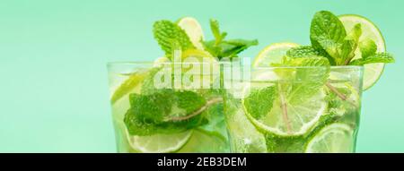 Rinfrescanti cocktail Mojito nei bicchieri a fette fresche lime e foglie di menta piperita su sfondo banner verde Foto Stock