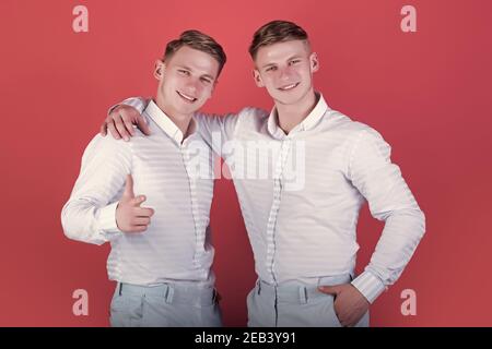 Concetto di fraternità e amicizia. Uomini felici che abbracciano. Due fratelli sorridenti e puntano il dito. Modelli su sfondo rosso. Gemelli blu Foto Stock