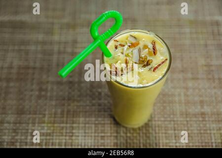 Lassi di mango fresco fatto in casa con noci e paglia sul tavolo. Dolce Mango Lassi,bevanda estiva fredda Foto Stock