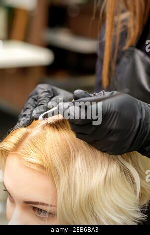 Una testa closeup di una giovane bionda che riceve tintura capelli in un salone di parrucchiere Foto Stock