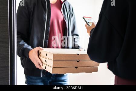 Consegna della pizza alla porta di casa dopo l'ordine online con il telefono cellulare. Il deliverer ha in mano scatole per fast food e il cliente utilizzando l'app per smartphone per pagare o mancia. Foto Stock