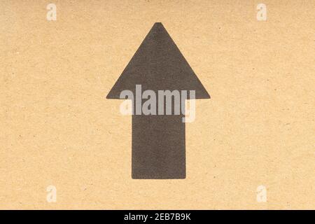 Freccia nera rivolta verso l'alto su sfondo di cartone marrone. Primo piano Foto Stock