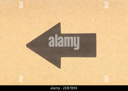 Freccia nera che punta a sinistra su sfondo di cartone marrone. Primo piano Foto Stock