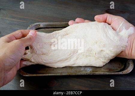 Le mani dell'uomo allungano l'impasto lievitato per cuocere il pane fatto in casa o pizza Foto Stock