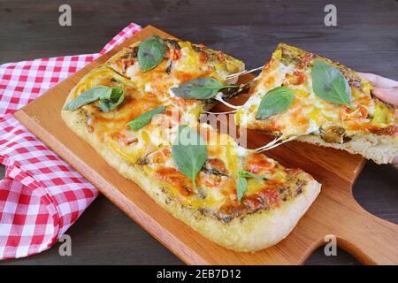 Fetta di appetitosa pesto veggie pizza con stretching formaggio essere preso da breadboard Foto Stock