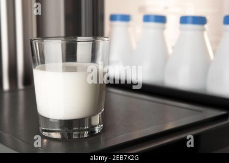 Primo piano di un bicchiere di latte sullo sportello del frigorifero con un gruppo di bottiglie di plastica conservate e allineate sullo sfondo. Il calcio è buono per la vostra salute Foto Stock