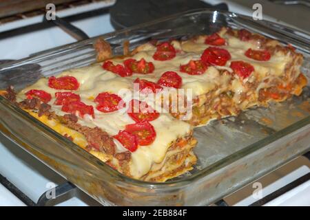 lasagne cotte al forno con pomodori ciliegini in teglia di vetro, su stufa a gas grattugiata Foto Stock