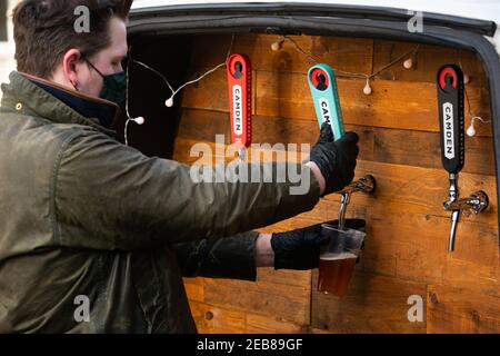 George Dean, ex bar manager, versa una pinta con il suo "Pub-on-WHEELS" a Clapham, a sud di Londra. George e Finn guidano alle porte della gente per versare loro le pinte e generare più di un'esperienza del pub che le lattine nei loro soggiorni. Data immagine: Venerdì 12 febbraio 2021. Foto Stock