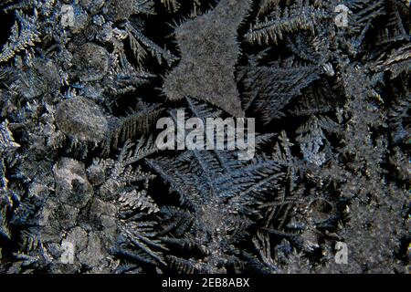 Macro di varie forme astratte di cristalli di ghiaccio su un finestra in vetro con sfondo nero Foto Stock