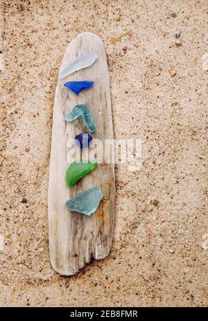 Diverso colore blu, verde, bianco vetro di mare o vetro di spiaggia su driftwood in spiaggia su sabbia. Il vetro è usato per essere pezzi di bottiglia e ora il mare è tumbled. Foto Stock