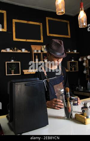 Il barista indonesiano prepara bevande al caffè per i clienti. Ritratto di un dipendente del bar che prepara il caffè al bar. Il processo di Foto Stock