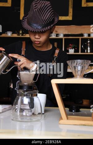 Il barista indonesiano prepara bevande al caffè per i clienti. Ritratto di un dipendente del bar che prepara il caffè al bar. Il processo di Foto Stock