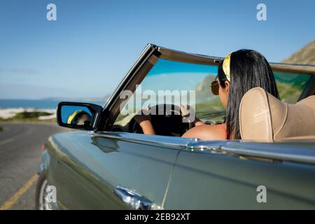 Donna mista che guida il giorno di sole in auto convertibile tenuta della ruota motrice Foto Stock