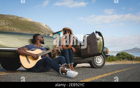 Diverse coppie che prendono una pausa sulla strada nella giornata di sole accanto alla convertibile auto l'uomo che suona la chitarra Foto Stock