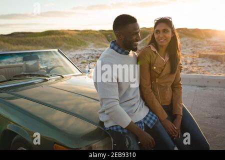 Coppia diversa seduta su un'auto convertibile che guarda ciascuno altro e sorridente Foto Stock