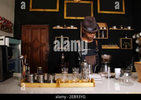 Il barista indonesiano prepara bevande al caffè per i clienti. Ritratto di un dipendente del bar che prepara il caffè al bar. Il processo di Foto Stock