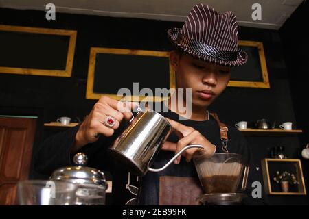 Il barista indonesiano prepara bevande al caffè per i clienti. Ritratto di un dipendente del bar che prepara il caffè al bar. Il processo di Foto Stock