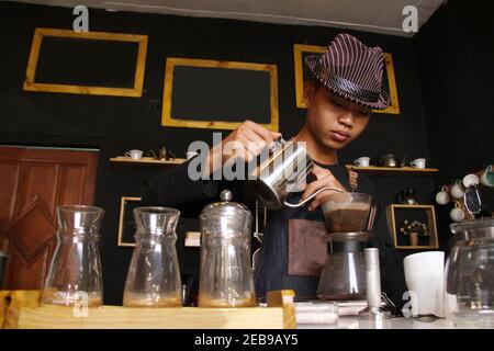 Il barista indonesiano prepara bevande al caffè per i clienti. Ritratto di un dipendente del bar che prepara il caffè al bar. Il processo di Foto Stock