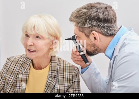 ENT medico che controlla l'orecchio femminile anziano usando un otoscopio. Esame uditivo per donna anziana. Otite media, infiammazione dell'orecchio Foto Stock