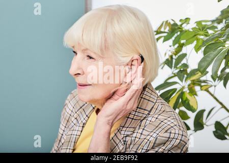 Concetto di trattamento per la perdita dell'udito nelle persone anziane. La donna anziana con apparecchio acustico dietro l'orecchio ascolta i suoni dell'ambiente Foto Stock