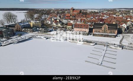 Waren, Germania. 12 Feb 2021. Coperto di ghiaccio e neve è il porto della città di Waren presso la Binnenmüritz, parte settentrionale della Müritz. Il permafrost ha ora causato il congelamento del più grande lago interno e dei laghi adiacenti del distretto dei laghi di Meclemburgo. Il ghiaccio sul Müritz di 117 chilometri quadrati è di circa 10 e 15 centimetri di spessore. (Foto aerea con un drone/copter) Credit: Bernd Wüstneck/dpa-Zentralbild/ZB/dpa/Alamy Live News Foto Stock