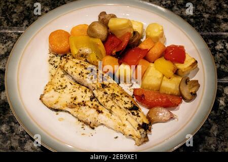 Spigola cotta con verdure arrostite su un piatto, dieta sana; pasto di spigola con peperoni arrosto, carote, pastinache, funghi e aglio; UK Foto Stock
