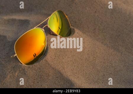 Occhiali da sole a specchio da vicino sulla spiaggia di sabbia con tramonto e riflessi di coppia. Occhiali da sole riflettenti sulla sabbia in spiaggia in estate sera. Vacanza estiva Foto Stock