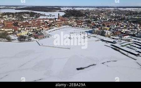 Waren, Germania. 12 Feb 2021. Coperto di ghiaccio e neve è il porto della città di Waren presso la Binnenmüritz, parte settentrionale della Müritz. Il permafrost ha ora causato il congelamento del più grande lago interno e dei laghi adiacenti del distretto dei laghi di Meclemburgo. Il ghiaccio sul Müritz di 117 chilometri quadrati è di circa 10 e 15 centimetri di spessore. (Foto aerea con un drone/copter) Credit: Bernd Wüstneck/dpa-Zentralbild/ZB/dpa/Alamy Live News Foto Stock