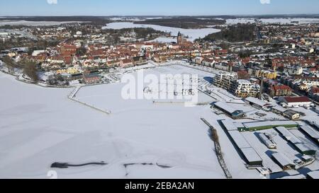 Waren, Germania. 12 Feb 2021. Coperto di ghiaccio e neve è il porto della città di Waren presso la Binnenmüritz, parte settentrionale della Müritz. Il permafrost ha ora causato il congelamento del più grande lago interno e dei laghi adiacenti del distretto dei laghi di Meclemburgo. Il ghiaccio sul Müritz di 117 chilometri quadrati è di circa 10 e 15 centimetri di spessore. (Foto aerea con un drone/copter) Credit: Bernd Wüstneck/dpa-Zentralbild/ZB/dpa/Alamy Live News Foto Stock