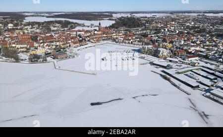 Waren, Germania. 12 Feb 2021. Coperto di ghiaccio e neve è il porto della città di Waren presso la Binnenmüritz, parte settentrionale della Müritz. Il permafrost ha ora causato il congelamento del più grande lago interno e dei laghi adiacenti del distretto dei laghi di Meclemburgo. Il ghiaccio sul Müritz di 117 chilometri quadrati è di circa 10 e 15 centimetri di spessore. (Foto aerea con un drone/copter) Credit: Bernd Wüstneck/dpa-Zentralbild/ZB/dpa/Alamy Live News Foto Stock
