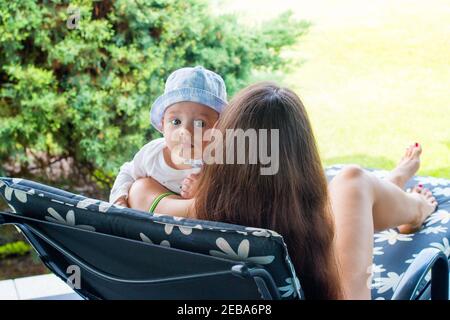 Bambino nelle braccia della madre, madre nuova che riposa con un bambino di 5 mesi su una sedia del ponte Foto Stock