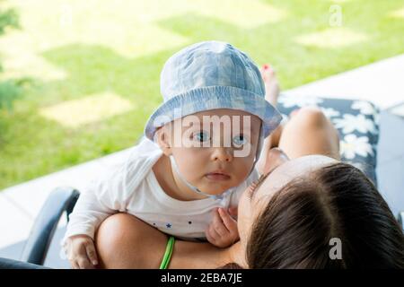 Bambino che riposa sopra la spalla della madre e guarda fuori con occhi blu focalizzati espressione curiosa Foto Stock