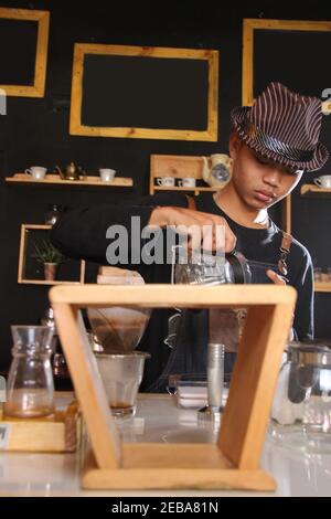 Il barista indonesiano prepara bevande al caffè per i clienti. Ritratto di un dipendente del bar che prepara il caffè al bar. Il processo di Foto Stock