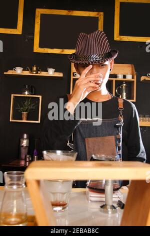 Il barista indonesiano prepara bevande al caffè per i clienti. Ritratto di un dipendente del bar che prepara il caffè al bar. Il processo di Foto Stock