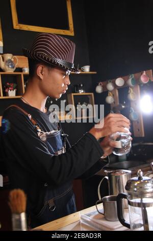 Il barista indonesiano prepara bevande al caffè per i clienti. Ritratto di un dipendente del bar che prepara il caffè al bar. Il processo di Foto Stock