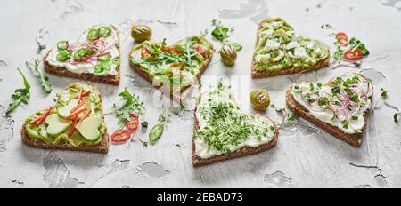 Crostini gourmet a forma di cuore, tapas o cicchetti su pane sano di segale per i valentini condito con pera di avocado e erbe e spezie fresche assortite Foto Stock
