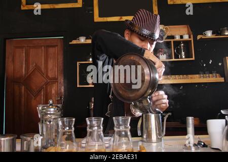 Il barista indonesiano prepara bevande al caffè per i clienti. Ritratto di un dipendente del bar che prepara il caffè al bar. Il processo di Foto Stock