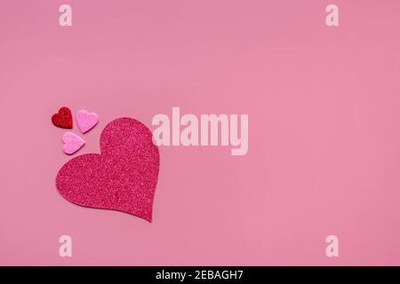 Grande cuore rosso e piccoli cuori rossi, rosa, viola e viola in carta isolata su sfondo rosa con spazio copia. Decorazione per San Valentino Foto Stock