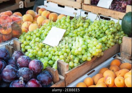 Grappoli d'uva, pesche e prugne sul banco. I grappoli verdi e rossi di uve mature sono disposti al banco del mercato agricolo. La frutta Foto Stock