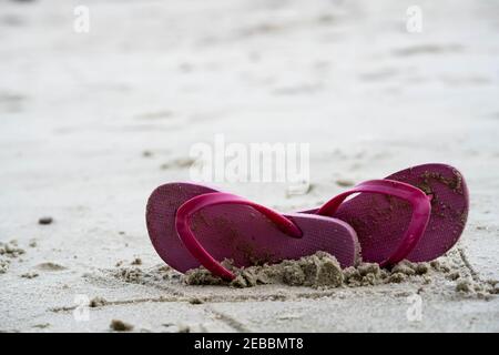 Estate vacanza spiaggia sfondo con flip flop su una spiaggia tropicale. Pantofole rosse da una sabbia su una spiaggia, concetto di relax Foto Stock