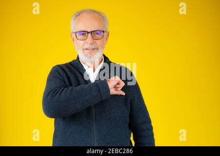 Uomo alto bello grigio-capelli isolato mano sul petto gesto sopra sfondo giallo Foto Stock