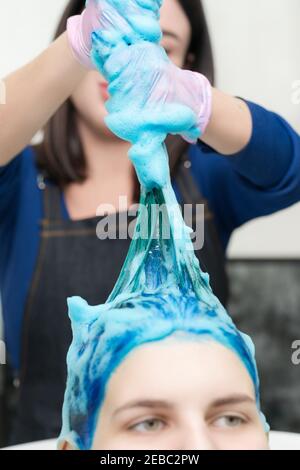 Professionale parrucchiera lava la testa femminile con il colore zaffiro dopo il processo di colorazione dei capelli. Lavare i capelli con shampoo in salone di bellezza. Foto Stock