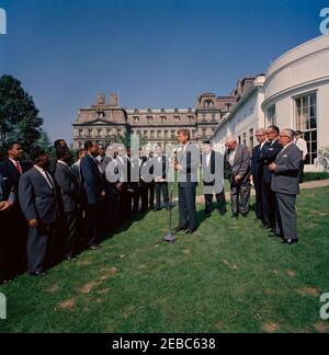 Visita dei partecipanti all'American Institute for Free Labor Management, ore 10:05. Il presidente John F. Kennedy (ai microfoni) trasmette osservazioni ai partecipanti al programma di formazione dell'American Institute for Free Labour Development (AIFLD) per i leader sindacali dell'America Latina e dei Caraibi; il partecipante Eric Lloyd Harris, della Giamaica (con cravatta ad arco), si trova al centro del gruppo. Alle spalle del presidente Kennedy a destra (L-R): Specialista dell'America Latina del Dipartimento del lavoro degli Stati Uniti, Joaquin A. Bazan, Jr.; presidente della Federazione americana del lavoro e del Congresso delle organizzazioni industriali Foto Stock