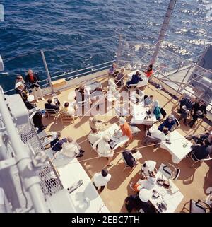 Il presidente Kennedy si accuda alla prima gara di Coppa Americau0027s. Il presidente John F. Kennedy e la First Lady Jacqueline Kennedy partecipano alla prima gara della Americau0027s Cup 1962 a bordo della USS Joseph P. Kennedy, Jr., al largo della costa di Newport, Rhode Island. Il presidente Kennedy (seduto sullo sfondo centrale, guardando attraverso il binocolo) guarda la corsa; la signora Kennedy (seduta a sinistra) visita con il capo del protocollo, Angier Biddle Duke. Anche nella foto: Naval Aide al Presidente, Capitano Tazewell Shepard; Vice Segretario del Tesoro, James A. Reed; sotto Segretario della Marina, Paul u0022Redu0022 fa Foto Stock