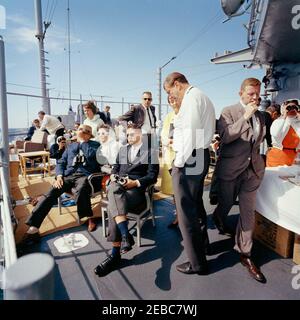 Il presidente Kennedy si accuda alla prima gara di Coppa Americau0027s. Il presidente John F. Kennedy e la First Lady Jacqueline Kennedy partecipano alla prima gara della Americau0027s Cup 1962 a bordo della USS Joseph P. Kennedy, Jr., al largo della costa di Newport, Rhode Island. Il presidente Kennedy (sullo sfondo a sinistra, con occhiali da sole) parla con il rappresentante John E. Fogarty (Rhode Island); la signora Kennedy (a sinistra) visita con il capo del protocollo, Angier Biddle Duke (per lo più nascosto). Anche nella foto: Hugh D. Auchincloss; Janet Auchincloss; Nancy Joy Salinger (moglie del Segretario della stampa, Pierre Salinger); Janet Jennings Auchincl Foto Stock