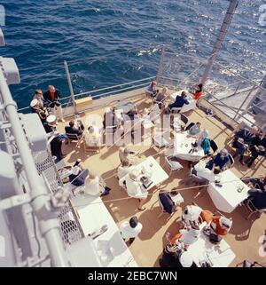 Il presidente Kennedy si accuda alla prima gara di Coppa Americau0027s. Il presidente John F. Kennedy e la First Lady Jacqueline Kennedy partecipano alla prima gara della Americau0027s Cup 1962 a bordo della USS Joseph P. Kennedy, Jr., al largo della costa di Newport, Rhode Island. Il presidente Kennedy (seduto sullo sfondo centrale, guardando attraverso il binocolo) guarda la corsa; la signora Kennedy (seduta a sinistra) visita con il capo del protocollo, Angier Biddle Duke. Anche nella foto: Naval Aide al Presidente, Capitano Tazewell Shepard; Vice Segretario del Tesoro, James A. Reed; sotto Segretario della Marina, Paul u0022Redu0022 fa Foto Stock