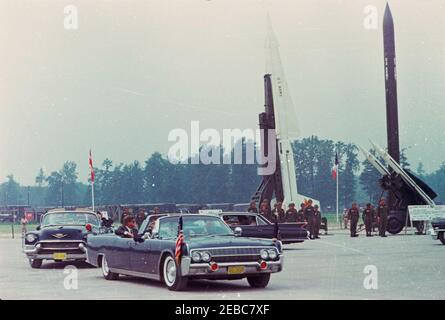 Viaggio in Europa: Germania, Hanau: Arrivo a Fliegerhorst Kaserne, indirizzo, e ispezione di truppe e attrezzature, 10:45. Il presidente John F. Kennedy (in prima macchina, indossando occhiali da sole) corre nella limousine presidenziale (Lincoln-Mercury Continental convertibile) durante un'ispezione di truppe militari e attrezzature a Fliegerhorst Kaserne a Hanau, Germania occidentale (Repubblica federale). [Graffi e difetti in tutta l'immagine sono originali al negativo.] Foto Stock