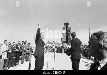 Presentazione della NASA (National Aeronautics and Space Administration) Distinguished Service Medal (DSM) all'astronauta John Herschel Glenn, Jr., a Cape Canaveral. L'astronauta tenente colonnello John H. Glenn, Jr. (A sinistra) ondeggia verso la folla di lavoratori riuniti al Launch Complex 14, prima della cerimonia di presentazione della sua Medaglia di Servizio della National Aeronautics and Space Administration (NASA); il presidente John F. Kennedy (con un elmetto, con ritorno alla telecamera) si trova a destra. Il pad e la torre di servizio da cui il tenente colonnello Glenn è stato sollevato in orbita sono visibili nel backgro Foto Stock